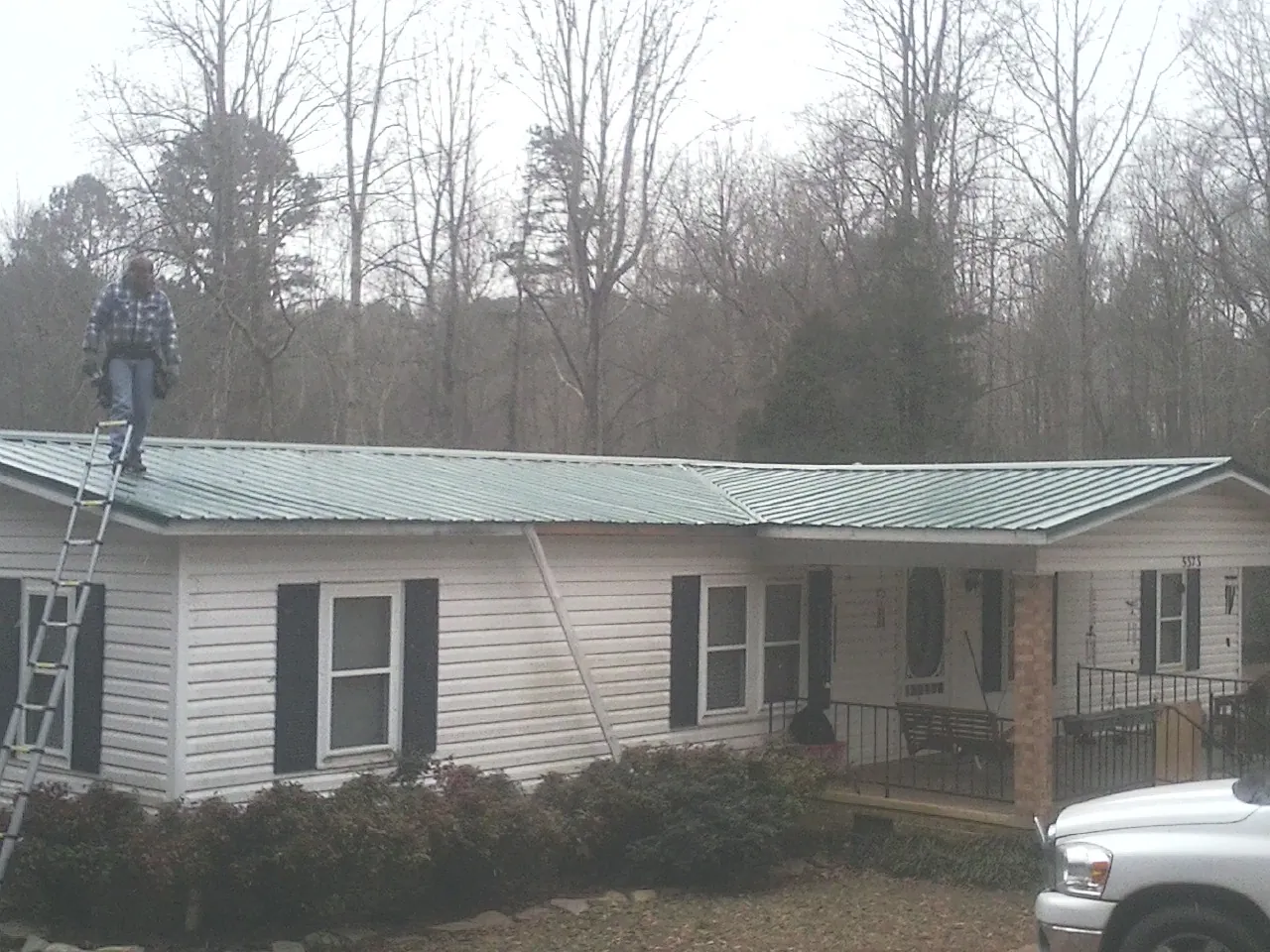 Worker on a ladder beside a new green metal roof on a ranch home in Tinley Park