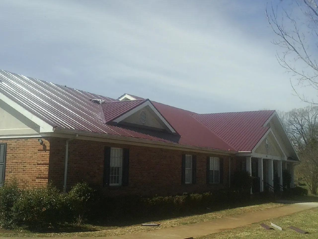 Red metal roof with gabled entries on a long brick building, from a Hail Damage Roof Repair job in Tinley Park