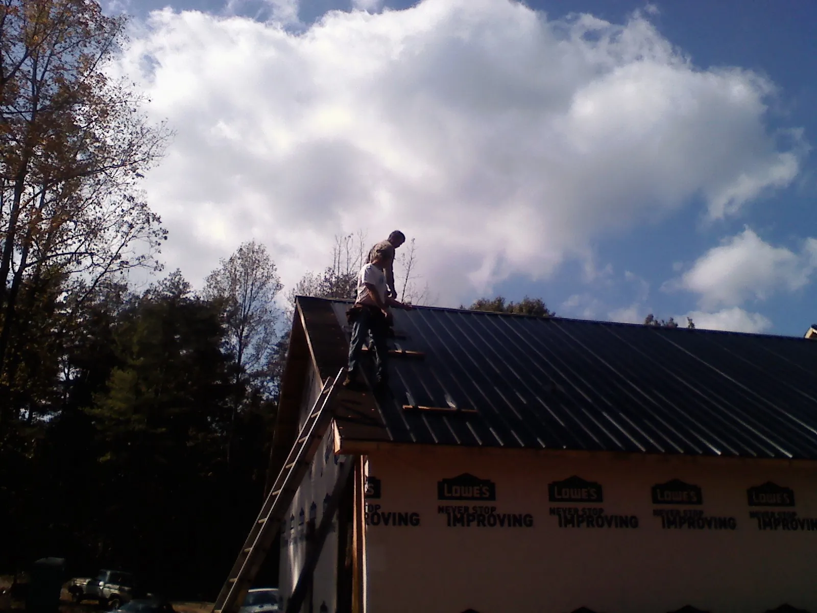 Roofer fastening dark metal panels high against a cloudy sky, from a Roof Inspection job in Tinley Park