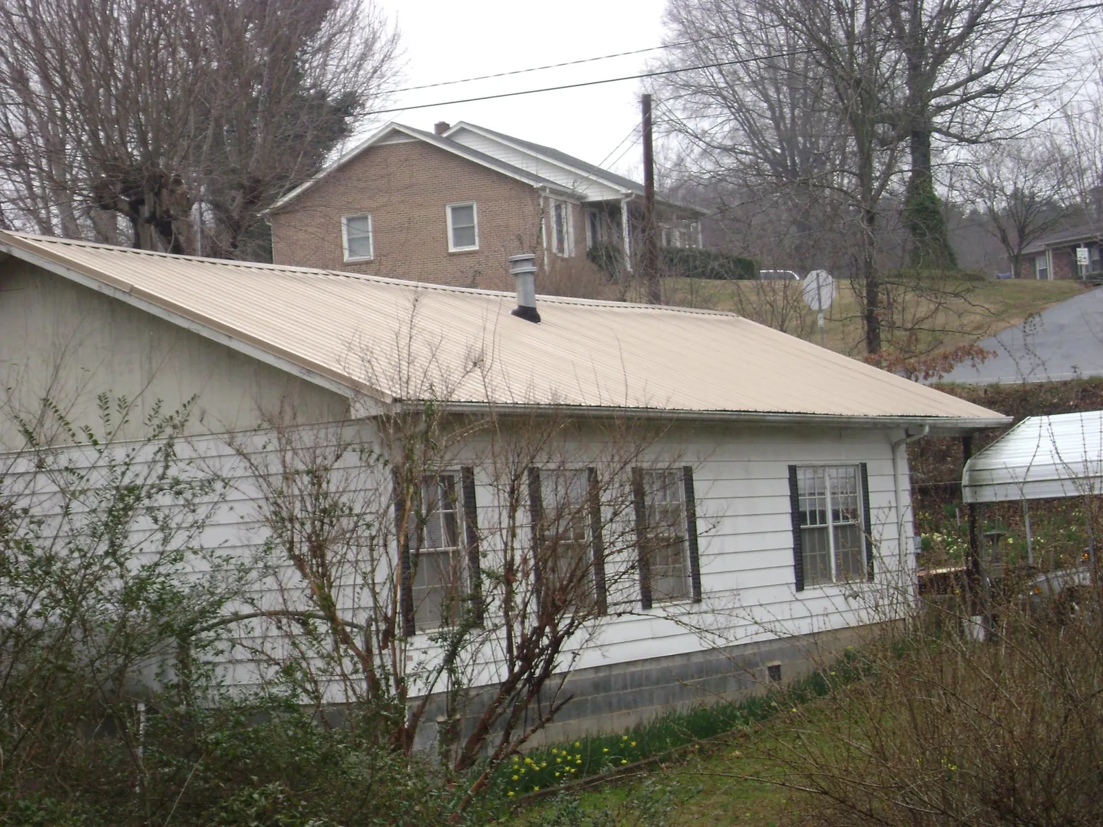 Tan metal roof on a white sided house set into a hillside — Commercial Roofing by Roofing Brothers in Tinley Park